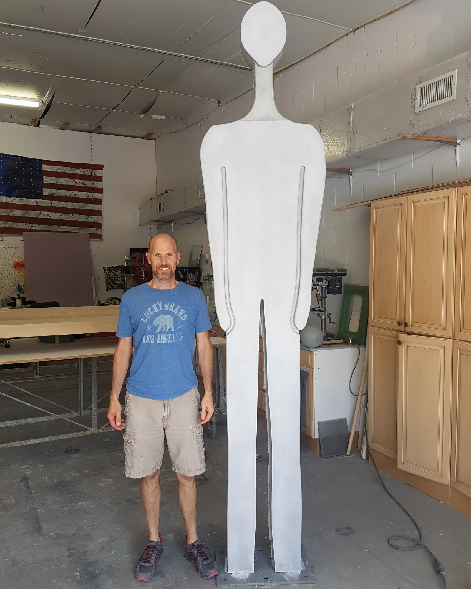 Douglas Lackey standing beside his tall concrete sculpture in the studio